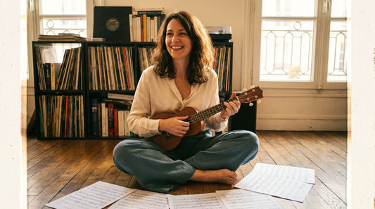 Femme jouant de la musique ukulélé chez elle, partitions autour d'elle, lumière chaude